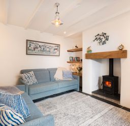 A living room with two blue sofas a wood burning stove and shelves with books and decorations at Kipper Cottage in Port Isaac