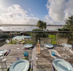 An outdoor dining table set with plates glasses and cutlery overlooking a garden pool and a body of water at Camel Point in Rock