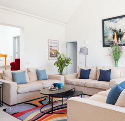 A living room with beige sofas and blue cushions a colorful rug and paintings on the wall at Landers Field in Rock