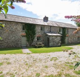 A stone house with a table and bench in the garden at Orchard Cottage in Polzeath