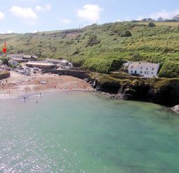 A coastal bay with green hillside and houses overlooking a small beach with boats and people at Stop Tide in Port Isaac