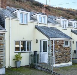The exterior of a two-story house with cream walls, stone accents, dormer windows, and a railing in front at Stop Tide Port Isaac