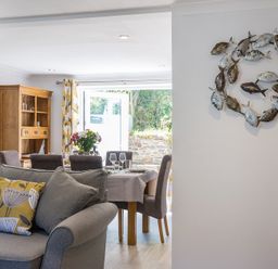 A dining area with a set table and a living room with a sofa and cushions at Stop Tide in Port Isaac