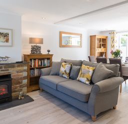 A living room with a gray sofa near a small fireplace and a dining table with chairs at Stop Tide in Port Isaac