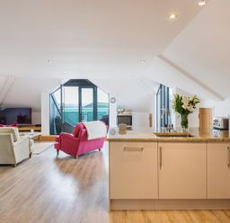 An open-plan kitchen and living room with a pink chair and beige armchairs near a TV and glass doors at Upper Deck in Rock