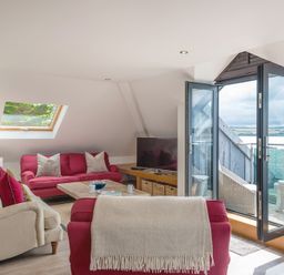 A living room with red and beige sofas a wooden coffee table and an open glass door leading to a balcony at Upper Deck in Rock