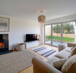 A living room with a sofa a fireplace a television and sliding glass doors at Elmwood in Port Isaac