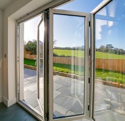 An open glass door leading to a patio and a fenced grassy area at Elmwood in Port Isaac