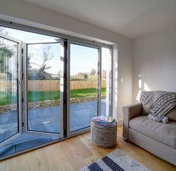 A living room with a beige sofa next to folding glass doors leading to a garden at Elmwood in Port Isaac