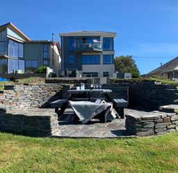 A stone patio with a picnic table and benches in front of modern houses at Egloskerry in New Polzeath