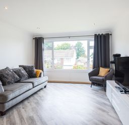 A living room with a grey sofa and armchair a television on a white console and a large window with curtains at Greenaway 4 Rockhaven Gardens in Rock