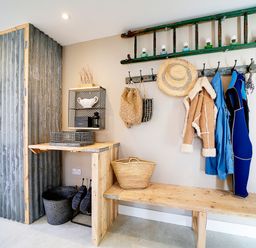 A mudroom with coats hanging on hooks a wooden bench a wooden cabinet with corrugated metal doors and baskets on the floor at Seahaven Port Isaac