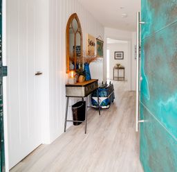 A hallway with a decorative mirror a lamp and vase on a console table and a blue front door at Seahaven in Port Isaac