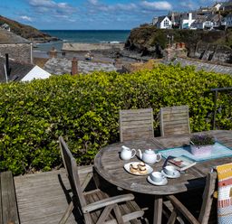 An outdoor wooden table with tea set and scones on a deck overlooking houses and the sea at Grey Roofs in Port Isaac