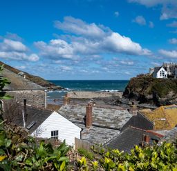 Rooftops of houses near a rocky coastline with the sea and partly cloudy sky at Grey Roofs in Port Isaac