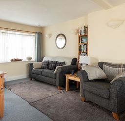 A living room with two grey sofas a wooden table a bookshelf and a window at Sea Glimpses in Port Isaac