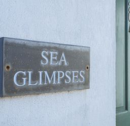 A metal sign reading sea glimpses on a white wall next to a green door at Sea Glimpses in Port Isaac
