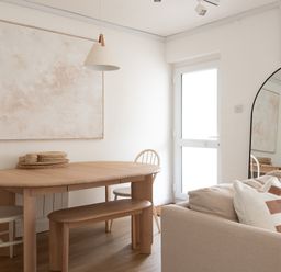 A dining area with a wooden table, chairs, a bench, a hanging light, a large mirror, and a sofa with pillows at Westward 8 Polzeath