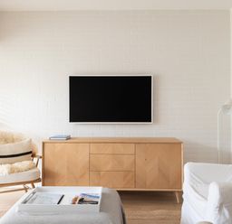 A living room with a mounted television a wooden media cabinet a white armchair and a wooden chair with a cushion at Westward 8 in Polzeath