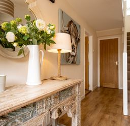 A hallway with a wooden console table holding a white pitcher with flowers and a lamp a wooden door and carpeted stairs at Flaad House in Rock