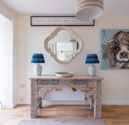 A wooden table with two blue lamps and a basket underneath a mirror and a painting of a cow at Flaad House in Rock