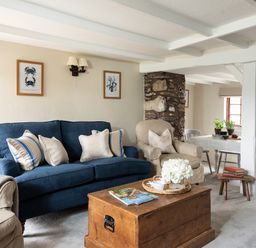 A living room with a blue sofa beige armchair wooden coffee table and dining table at Swallow Cottage in Port Isaac