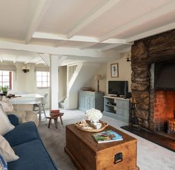 A living room with a blue couch a wooden coffee table a stone fireplace and a dining table at Swallow Cottage Port Isaac