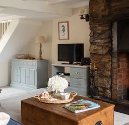 A living room with a stone fireplace a wooden coffee table a television and blue cabinets at Swallow Cottage in Port Isaac