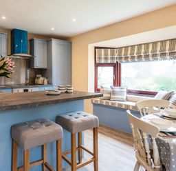 A kitchen with grey bar stools at a counter and a window seat with striped cushions at Brookside in Polzeath