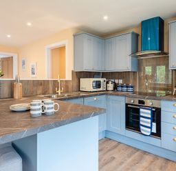 A kitchen with blue cabinets and a marble countertop with mugs and plates at Brookside in Polzeath