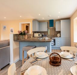 A kitchen and dining area with blue cabinets a dining table set and a couch at Brookside in Polzeath