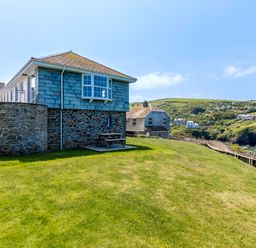 A house with stone walls and a small grassy yard near cliffs and the ocean at Gulland in Port Isaac
