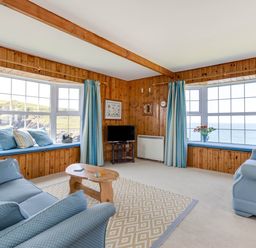 A living room with blue sofas wooden walls bay windows and a small wooden coffee table at Gulland in Port Isaac