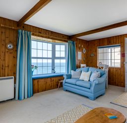A living room with wood panel walls a blue sofa and large windows overlooking the sea at Gulland in Port Isaac