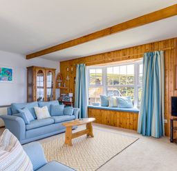 A living room with blue sofas a wooden coffee table and a bay window with cushions at Gulland in Port Isaac