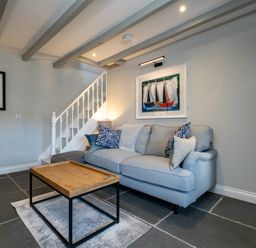 A living room with a light blue sofa and wooden coffee table under exposed ceiling beams at Mino Cottage in Port Isaac