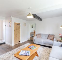 A living room with two gray sofas a wooden coffee table with books a floor lamp a side table with flowers and wooden doors at Bluebird Cottage in Newmarket