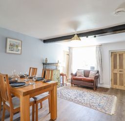 A dining area with a wooden table set with plates and glasses and a sitting area with a brown sofa and rug at Bluebird Cottage in Newmarket