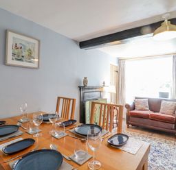 A dining room with wooden table set with plates and glasses next to a brown leather sofa with cushions at Bluebird Cottage in Newmarket