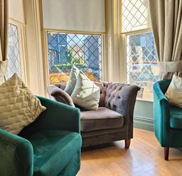 A sitting area with two green armchairs and a gray loveseat with cushions near leaded glass windows and beige curtains at Squirrel Lodge in Keswick