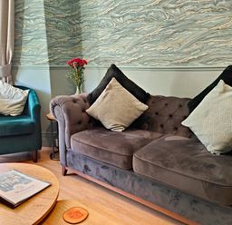 A living room with a grey sofa and teal armchair with cushions and a coffee table with magazines at Squirrel Lodge Keswick