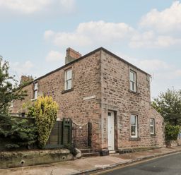 A corner view of a stone house with windows a door a black metal gate and bushes along a street at Islestone 1 Temperance Terrace in Berwick-Upon-Tweed