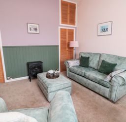 A living room with green sofas, an ottoman with a tea set, wooden closets, a small stove, and two framed pictures on the wall at Islestone 1 Temperance Terrace in Berwick-Upon-Tweed