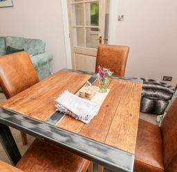 A dining area with a wooden table and brown chairs beside a green sofa at Islestone 1 Temperance Terrace in Berwick-Upon-Tweed