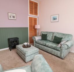 A living room with green sofas, an ottoman, a small stove, a floor lamp, and pictures on the walls at Islestone 1 Temperance Terrace in Berwick-Upon-Tweed