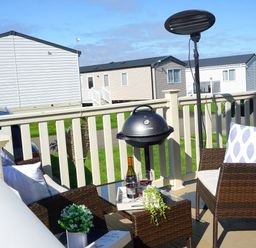 An outdoor patio with wicker chairs a table barbecue grill and a heater at Meadow Lodge in Cayton