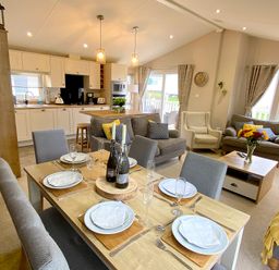 An open-plan dining and living area with a set dining table and a kitchen in the background at Meadow Lodge in Cayton