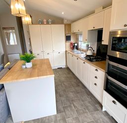 A kitchen with white cabinets wooden countertops a gas stove a microwave an oven a coffee maker and a small island with plants at Meadow Lodge in Cayton
