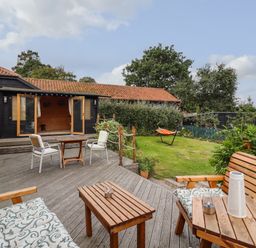 An outdoor wooden deck with chairs and tables leading to a garden with grass and a hammock at The Old Custom House in Wangford