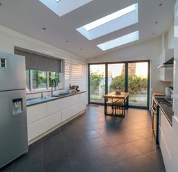 A kitchen with a refrigerator a sink a stove a wooden dining table with benches and large windows at South Bay House in Scarborough
